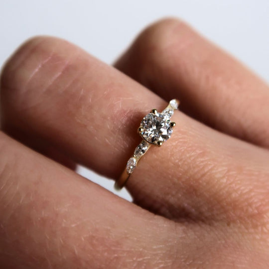 Juna Fae engagement ring in 18K recycled yellow gold, featuring a brilliant-cut center diamond with marquise-cut side stones, worn on finger.