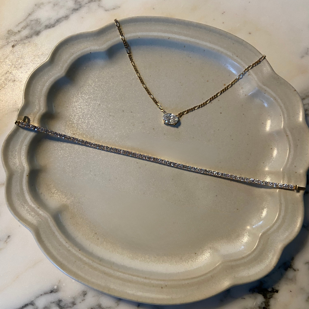 2 carat oval diamond necklaces in 18 carat yellow gold figaro chain and labgrown diamond tennis bracelet on a ceramic plate with a marble background
