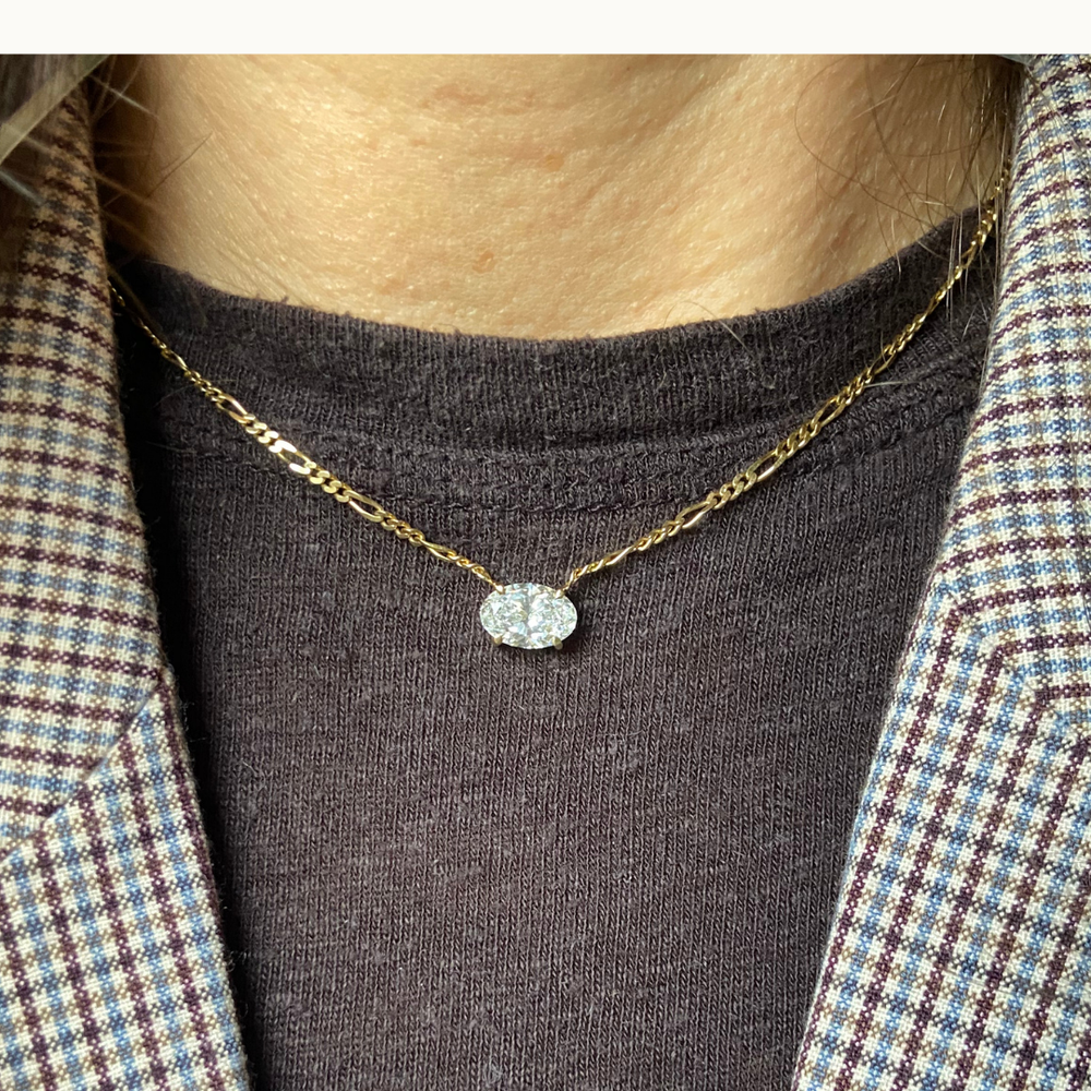 Model wearing 18 carat gold figaro chain necklace featuring a single solitaire 2 carat oval labgrown diamond pendant in a minimalist setting.