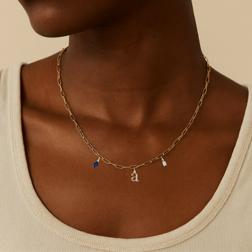 Model wearing 18 carat gold paperclip chain necklace featuring dangling gemstone charms, birthstone charm necklace and an initial or letter charm with labgrown diamonds on a chunky chain