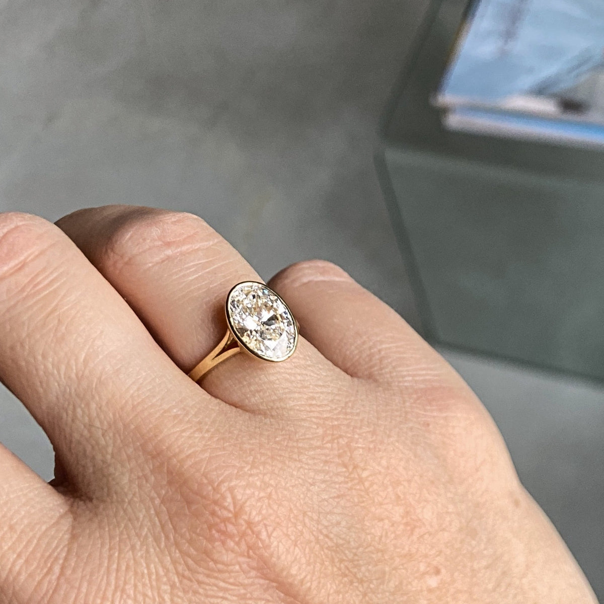 Aveline Ring worn on the hand, an oval lab-grown diamond in a gold bezel on a split shank, recycled 18K yellow gold