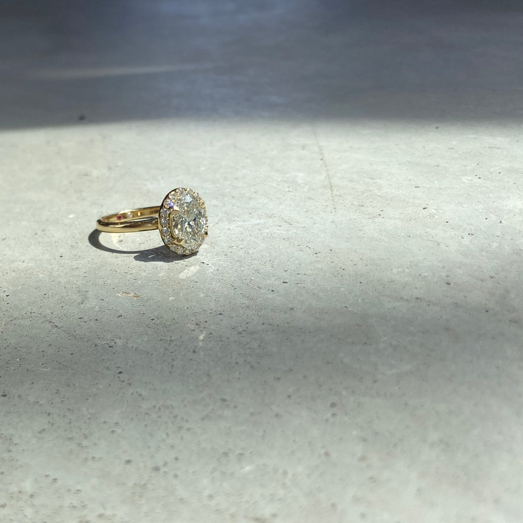 Dahlia Ring in sunlight on stone, an oval lab-grown diamond in a diamond halo, recycled 18K yellow gold