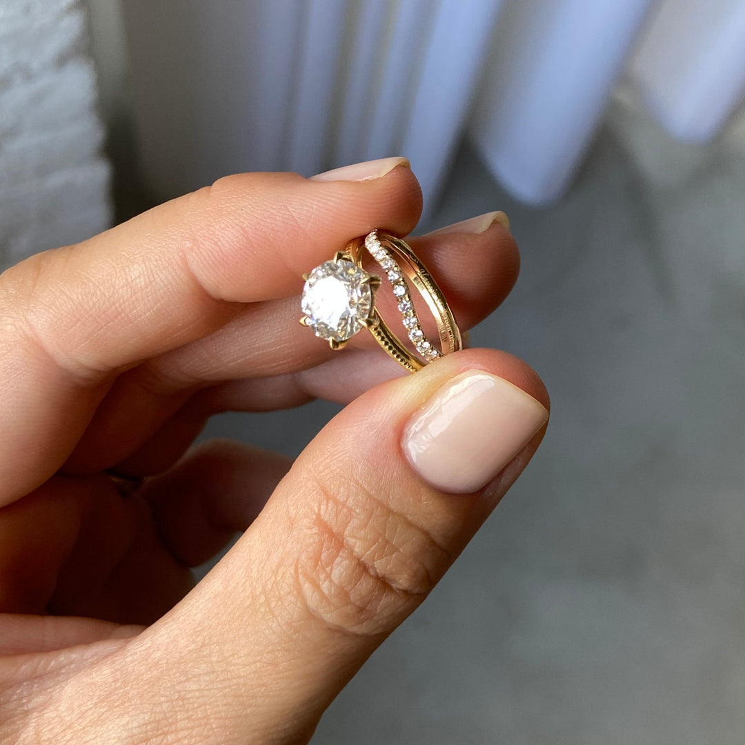 Laurel Solitaire stacked with diamond bands, held between the fingers, recycled 18K gold