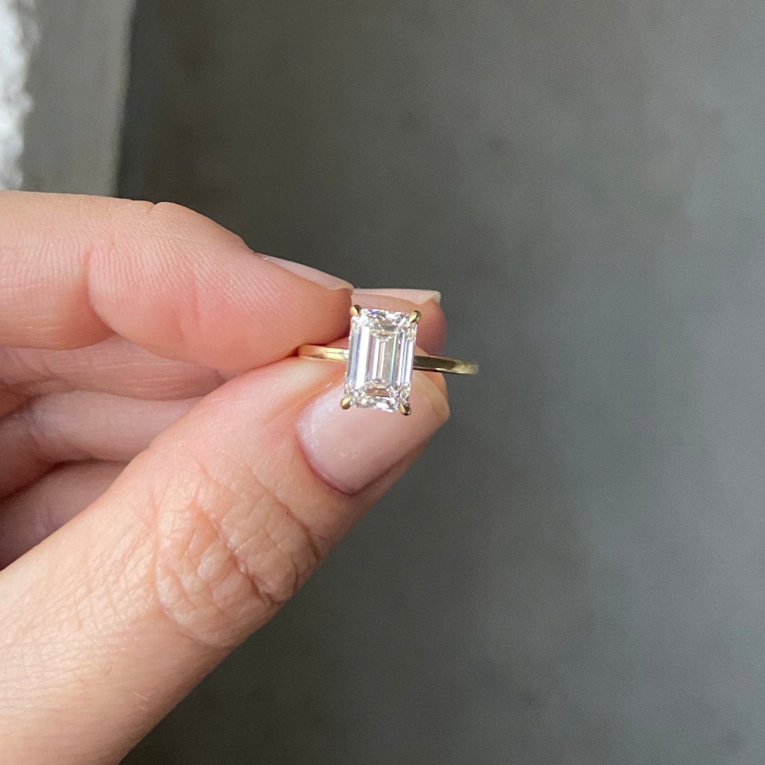 Primrose Emerald held between the fingers, an emerald-cut lab-grown diamond solitaire in recycled 18K yellow gold